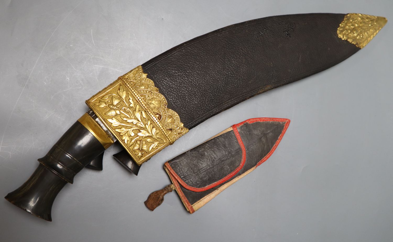 A kukri with skinning knives, leather sheath with elaborate embossed gilt metal mounts, blade 36cm